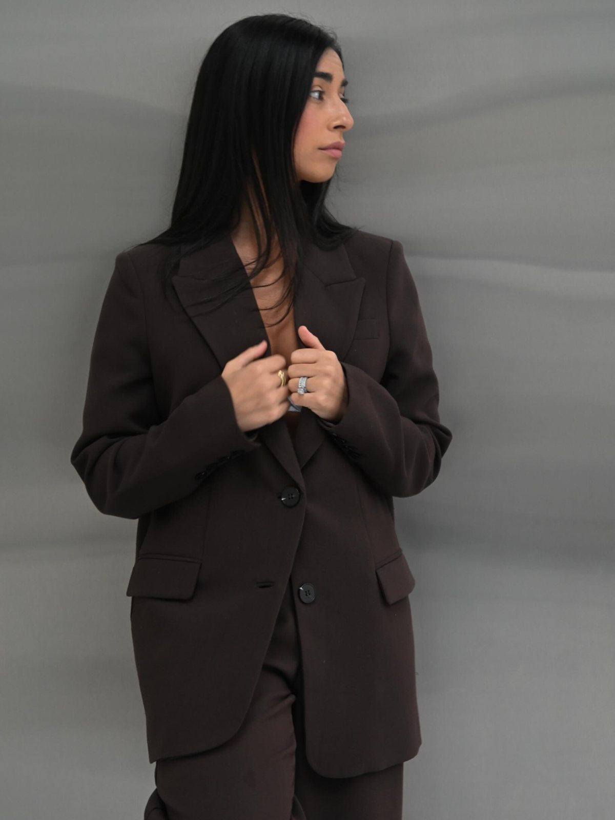 Steph, founder of Signed By G, in a brown suit against a grey backdrop
